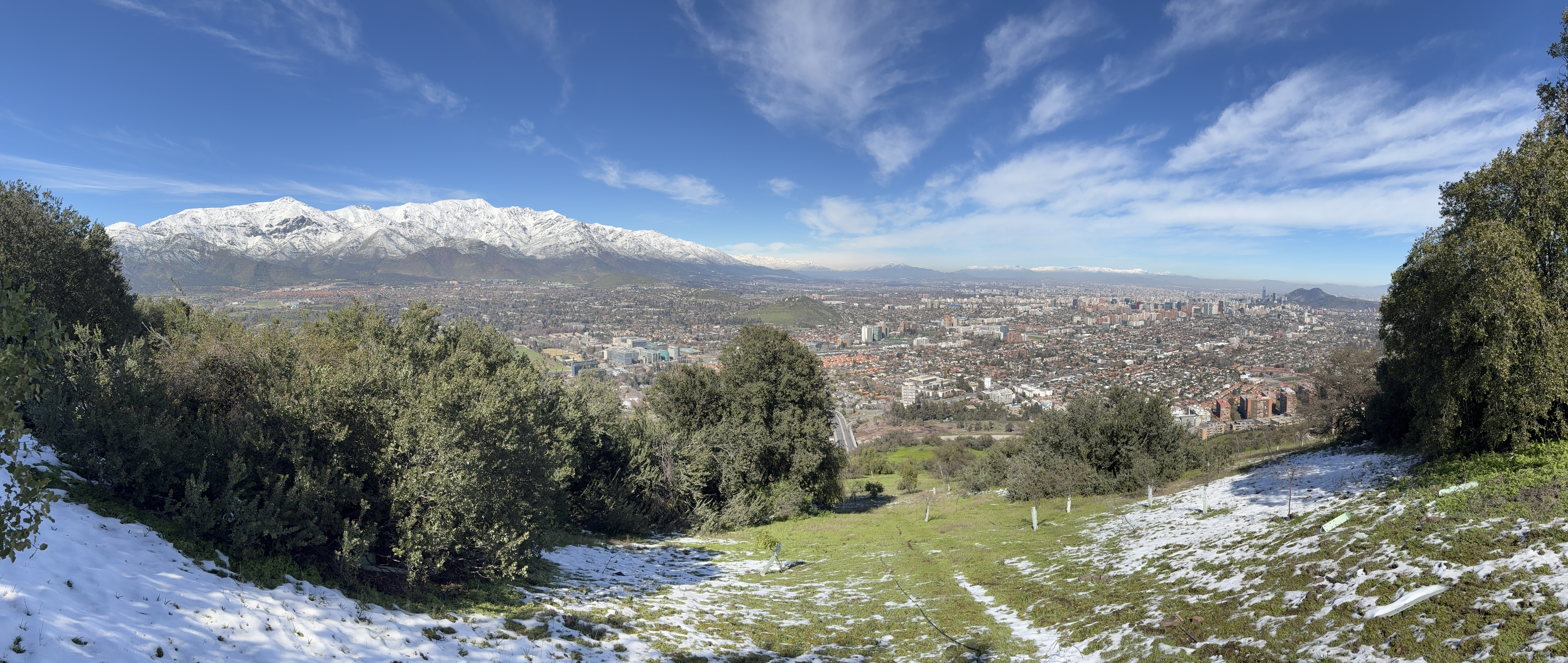 Panoramic view from Cerro Alvarado in Santiago, showcasing snow-capped mountains, lush greenery, and the urban landscape of the city below.